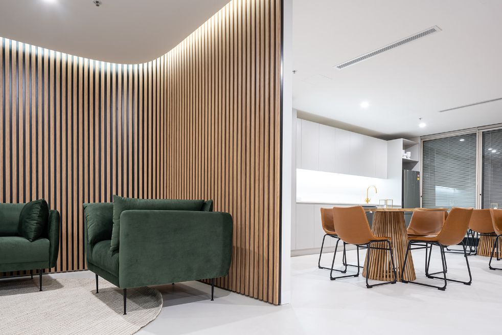 timber cladded wall with green chairs, with a bright white kitchen and tan chairs around a timber table