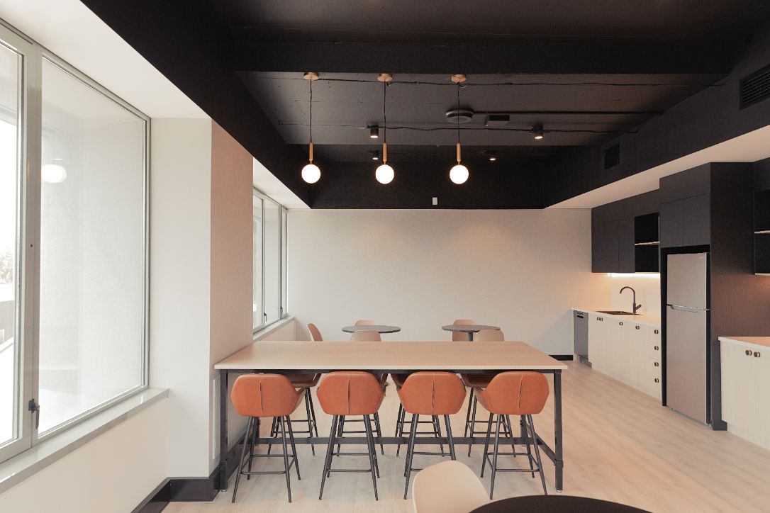 kitchen breakout space in an office featuring a high bar with tan chairs and pendant lights