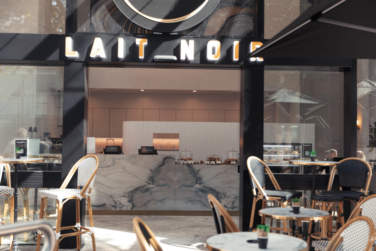 Cafe entrance image of Lait Noir showing tables and chairs outside looking inside to the stone countertop and cafe sign